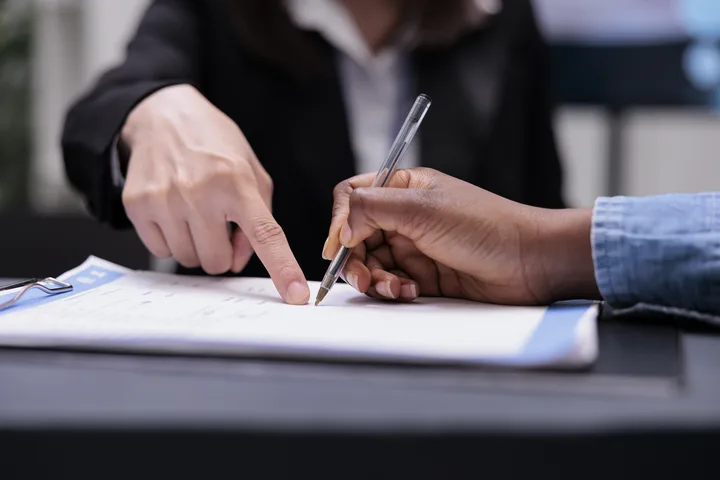 Responsável assinando com caneta o contrato de matrícula sobre uma prancheta, representando a formalização do contrato entre escola e família